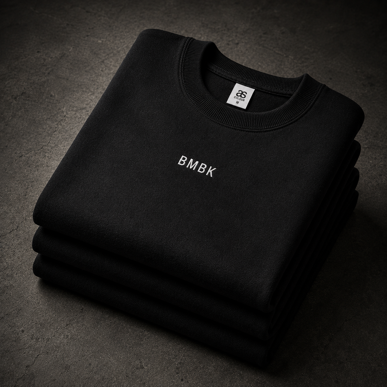 Stack of black sweatshirts with 'BMBK' branding on a dark surface