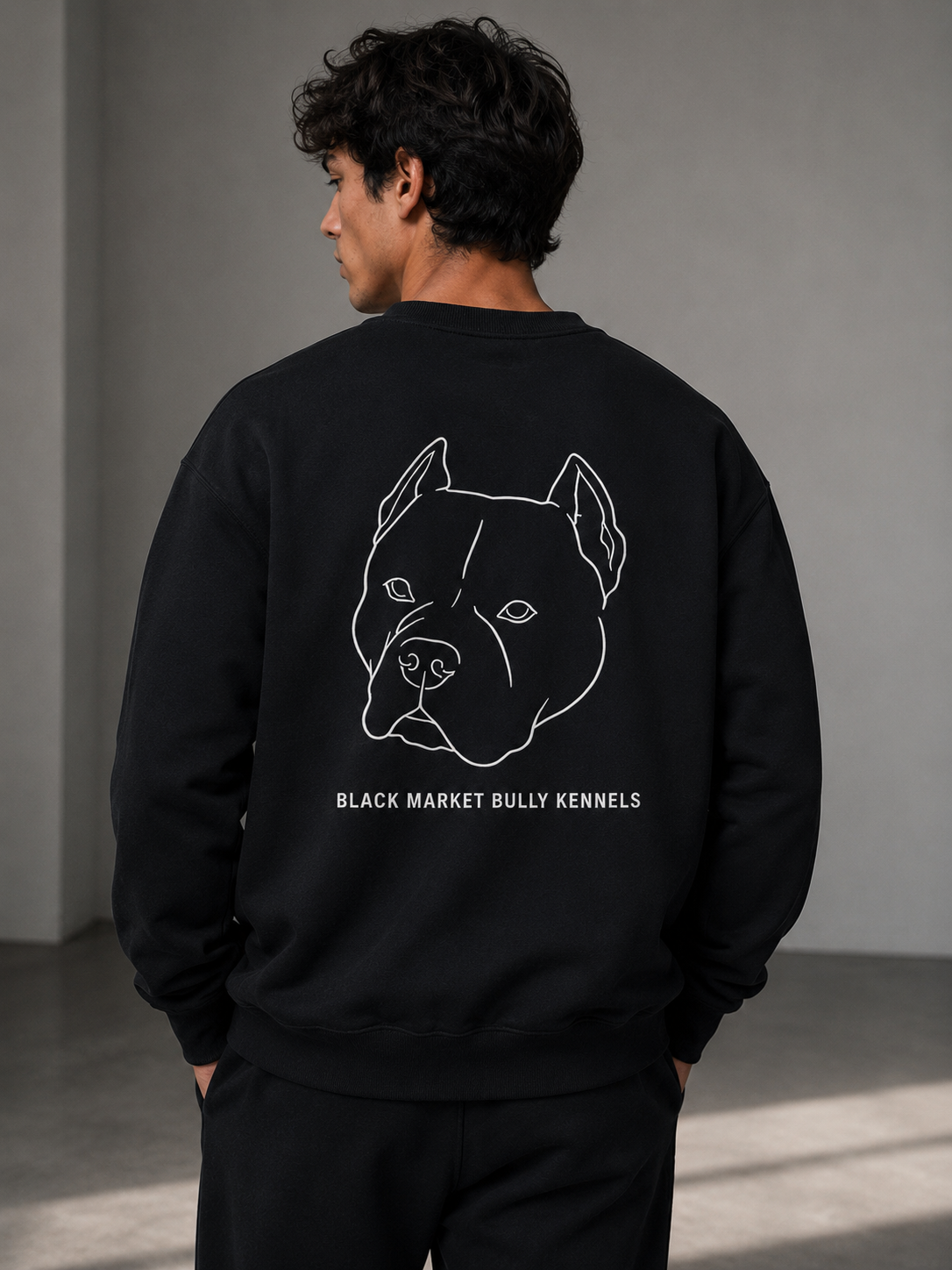 Person wearing a black sweatshirt with a dog illustration and text on the back, standing against a gray wall.
