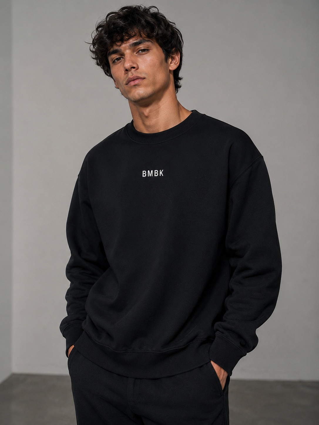 Man wearing a black sweatshirt with 'BMBK' logo against a gray background